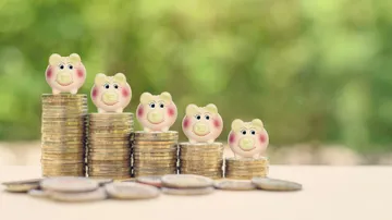 fünf Münzstapel mit darauf sitzenden Mini-Sparschweinen